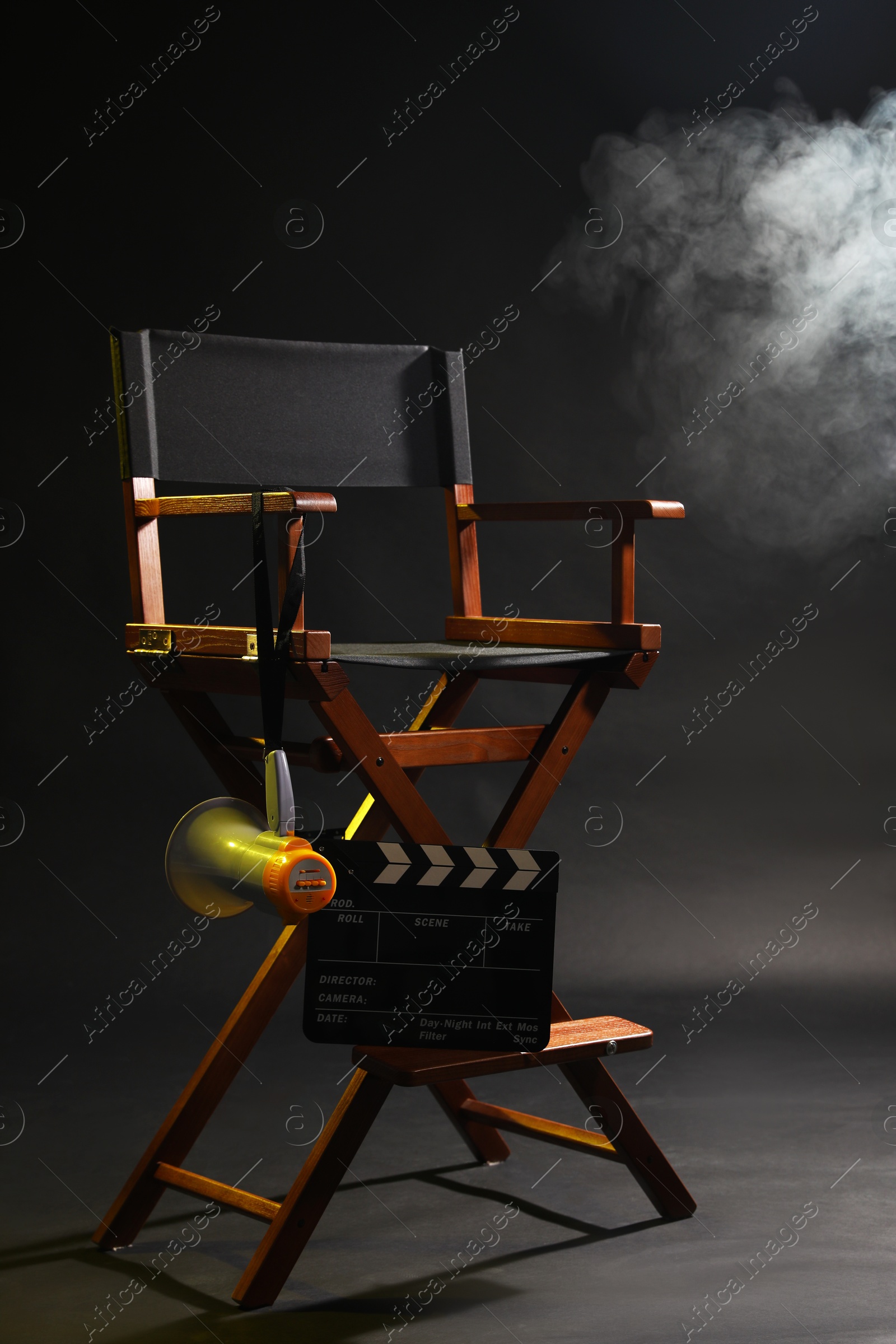 Photo of Director's chair with clapperboard and megaphone on dark background with smoke