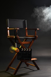 Photo of Director's chair with clapperboard and megaphone on dark background with smoke