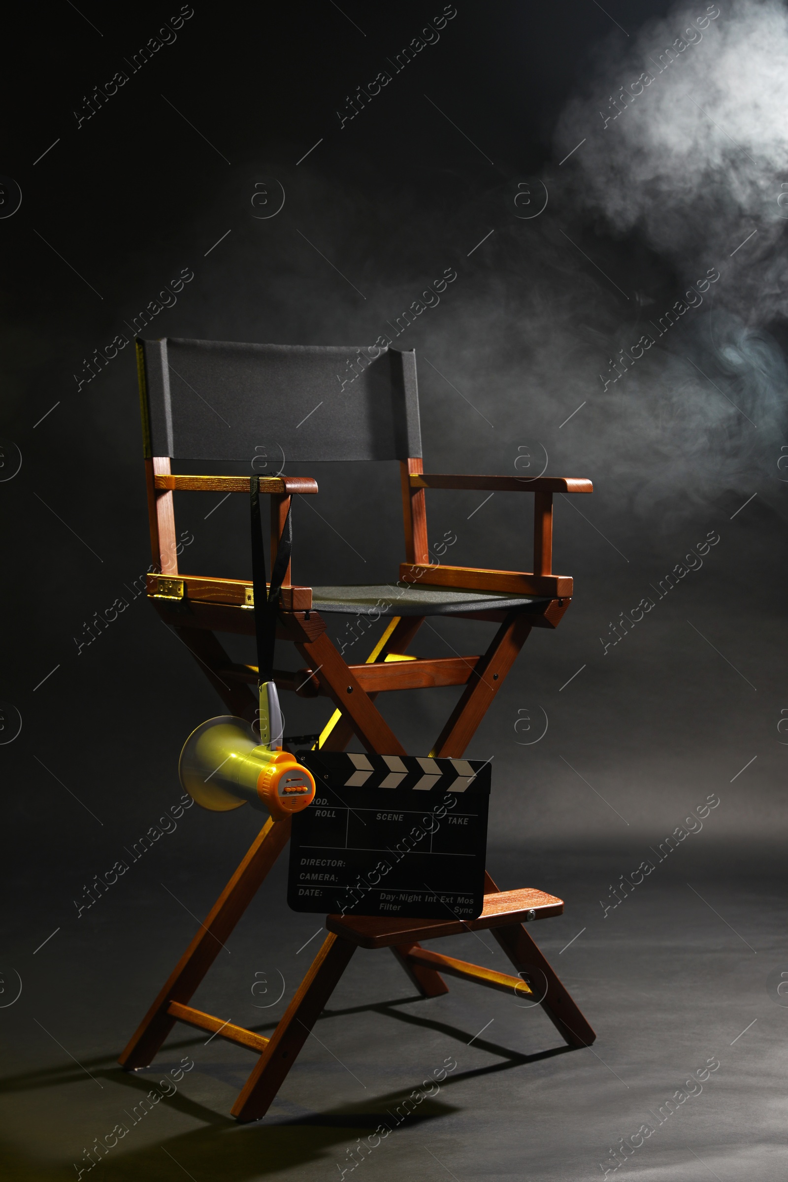 Photo of Director's chair with clapperboard and megaphone on dark background with smoke