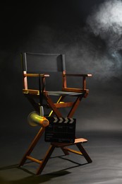 Photo of Director's chair with clapperboard and megaphone on dark background with smoke