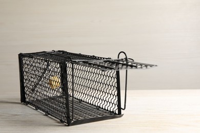 One metal mouse trap with bait on light wooden table. Space for text