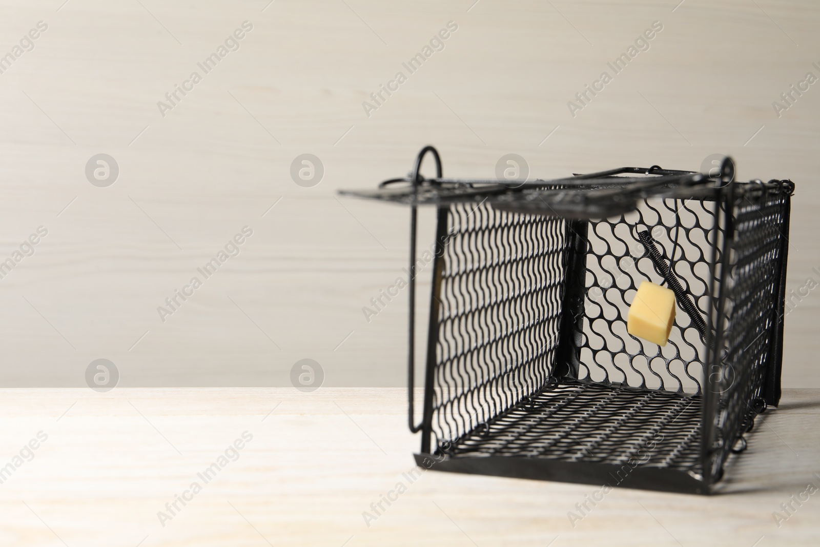 Photo of One metal mouse trap with bait on light wooden table. Space for text