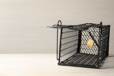 Photo of One metal mouse trap with bait on light wooden table. Space for text