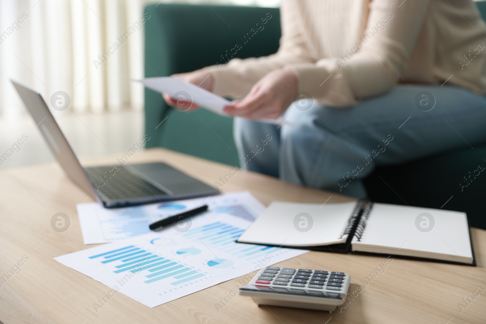 Photo of Budget. Woman with calculator, paperwork and laptop at wooden desk indoors, closeup