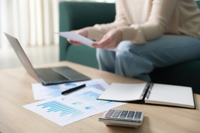 Photo of Budget. Woman with calculator, paperwork and laptop at wooden desk indoors, closeup