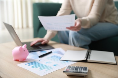 Photo of Budget. Woman with calculator, paperwork and laptop at wooden desk indoors, closeup