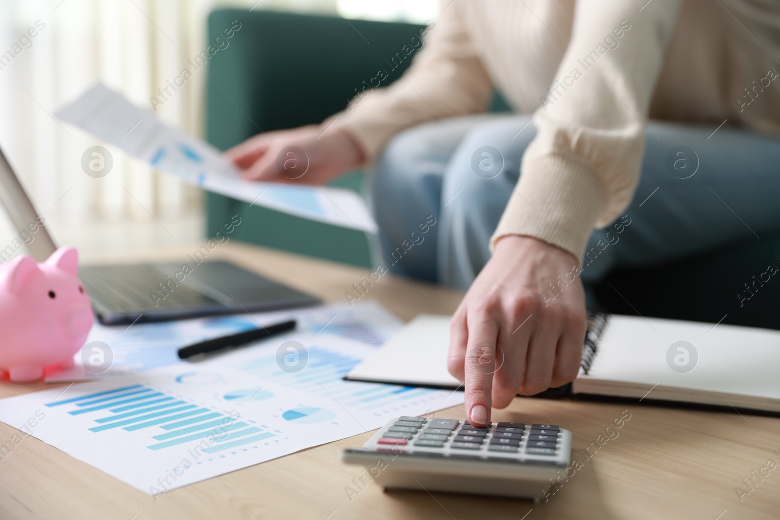 Photo of Budget. Woman with calculator, paperwork and laptop at wooden desk indoors, closeup