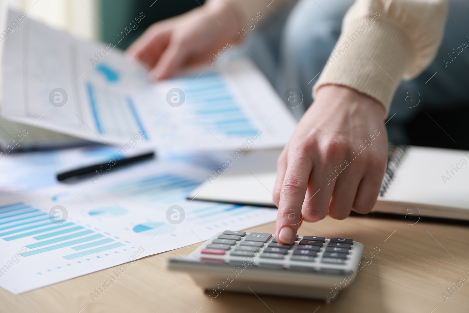 Photo of Budget. Woman with paperwork and calculator at wooden desk indoors, closeup