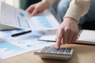 Photo of Budget. Woman with paperwork and calculator at wooden desk indoors, closeup