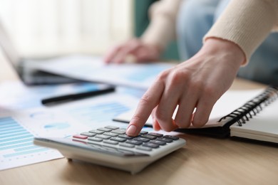 Photo of Budget. Woman with paperwork and calculator at wooden desk indoors, closeup