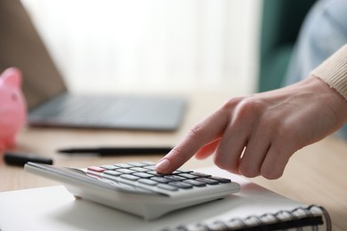 Photo of Budget. Woman with calculator, paperwork and laptop at wooden desk indoors, closeup