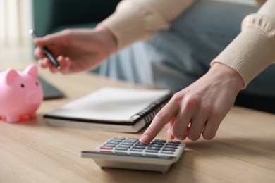 Photo of Budget. Woman with paperwork and calculator at wooden desk indoors, closeup