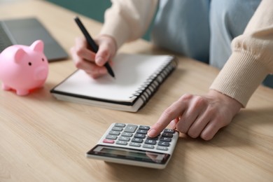 Photo of Budget. Woman with paperwork and calculator at wooden desk indoors, closeup