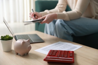 Photo of Budget. Woman with calculator, paperwork and laptop at wooden desk indoors, closeup