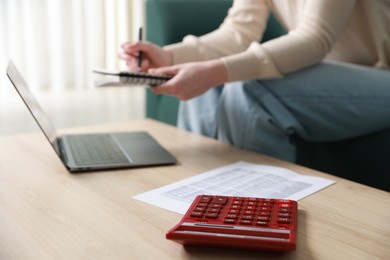 Photo of Budget. Woman with calculator, paperwork and laptop at wooden desk indoors, closeup