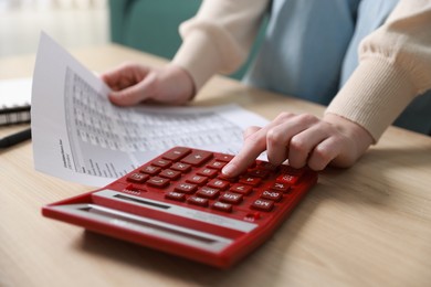 Photo of Budget. Woman with paperwork and calculator at wooden desk indoors, closeup