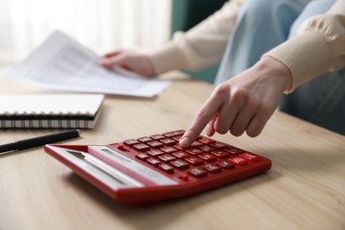 Photo of Budget. Woman with paperwork and calculator at wooden desk indoors, closeup