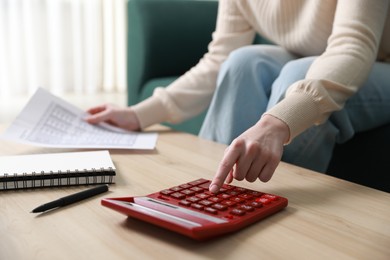 Photo of Budget. Woman with paperwork and calculator at wooden desk indoors, closeup