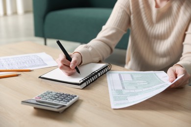 Photo of Budget. Woman with paperwork and calculator at wooden desk indoors, closeup