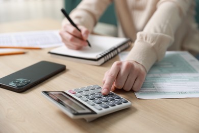 Photo of Budget. Woman with paperwork and calculator at wooden desk indoors, closeup