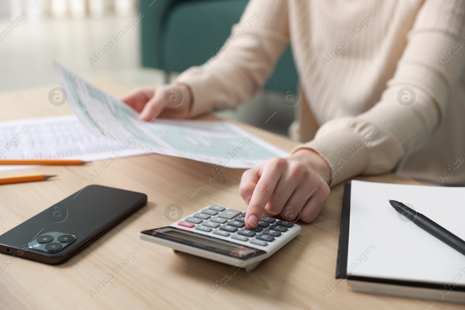 Photo of Budget. Woman with paperwork and calculator at wooden desk indoors, closeup