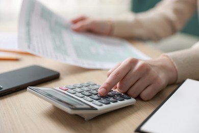 Photo of Budget. Woman with paperwork and calculator at wooden desk indoors, closeup