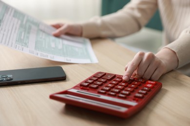 Photo of Budget. Woman with paperwork and calculator at wooden desk indoors, closeup