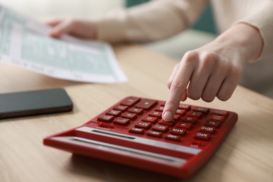 Photo of Budget. Woman with paperwork and calculator at wooden desk indoors, closeup