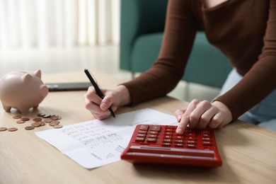 Photo of Budget. Woman with paperwork and calculator at wooden desk indoors, closeup