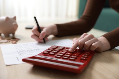 Photo of Budget. Woman with paperwork and calculator at wooden desk indoors, closeup