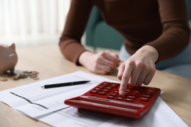 Photo of Budget. Woman with paperwork and calculator at wooden desk indoors, closeup