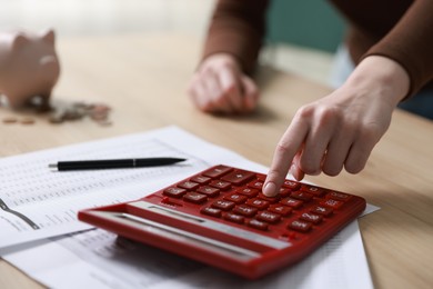 Photo of Budget. Woman with paperwork and calculator at wooden desk indoors, closeup