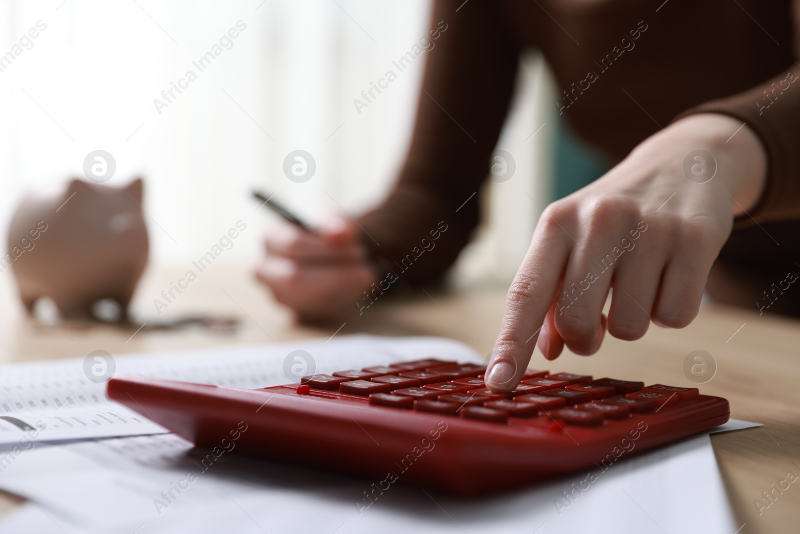 Photo of Budget. Woman with paperwork and calculator at wooden desk indoors, closeup