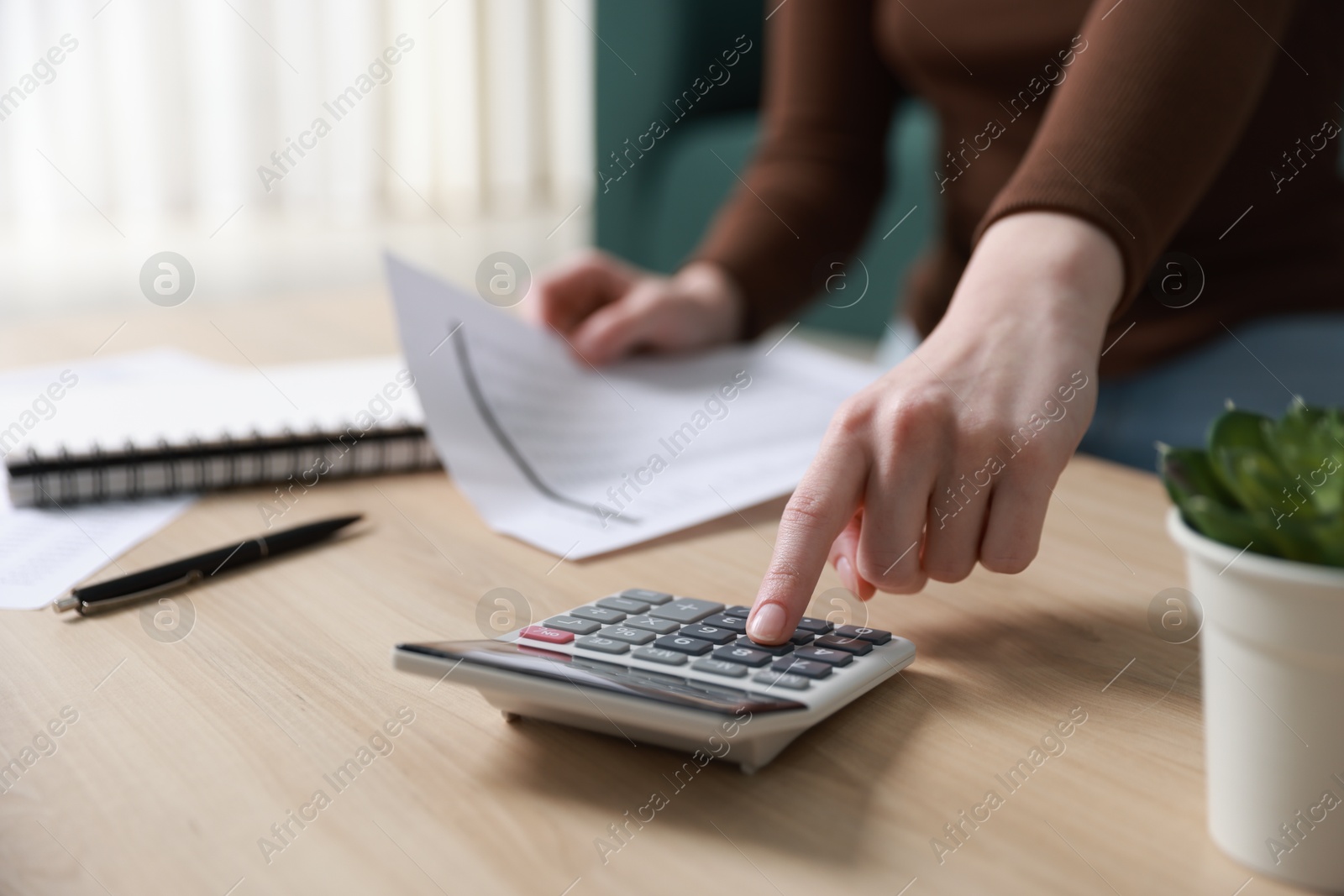 Photo of Budget. Woman with paperwork and calculator at wooden desk indoors, closeup