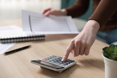 Photo of Budget. Woman with paperwork and calculator at wooden desk indoors, closeup