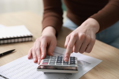 Photo of Budget. Woman with paperwork and calculator at wooden desk indoors, closeup