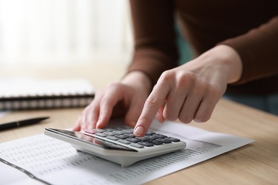 Photo of Budget. Woman with paperwork and calculator at wooden desk indoors, closeup