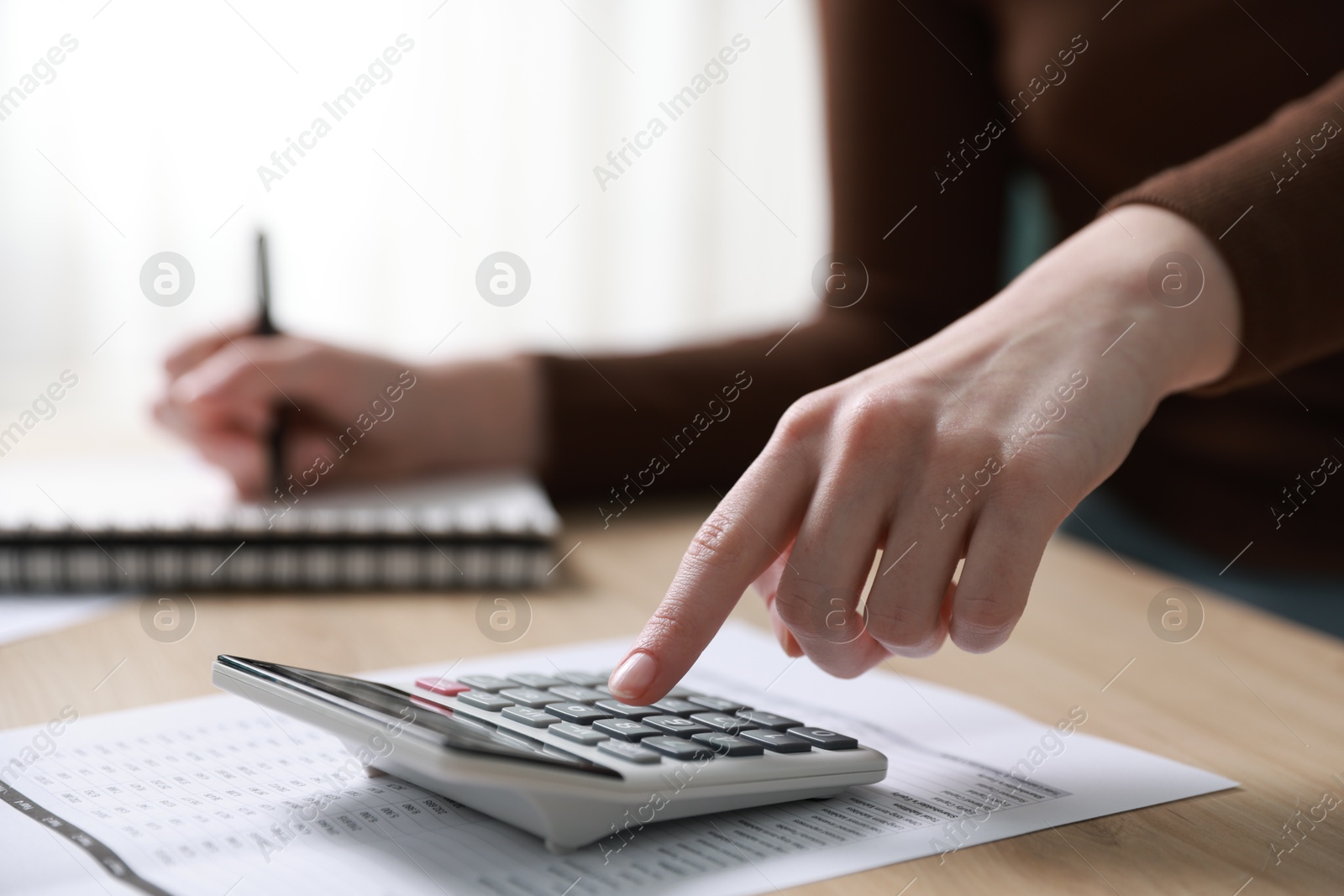 Photo of Budget. Woman with paperwork and calculator at wooden desk indoors, closeup