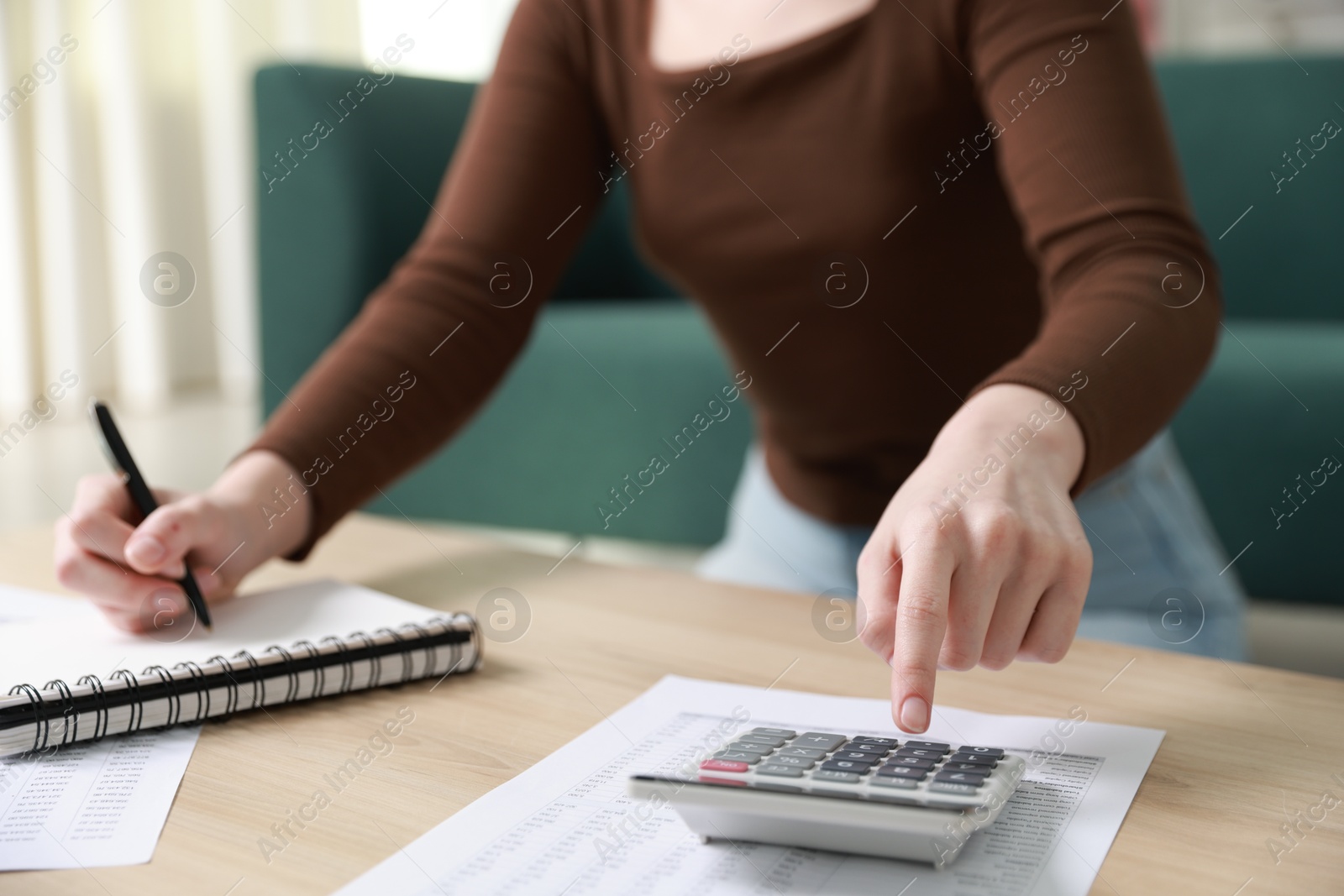 Photo of Budget. Woman with paperwork and calculator at wooden desk indoors, closeup