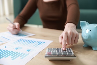 Photo of Budget. Woman with paperwork and calculator at wooden desk indoors, closeup