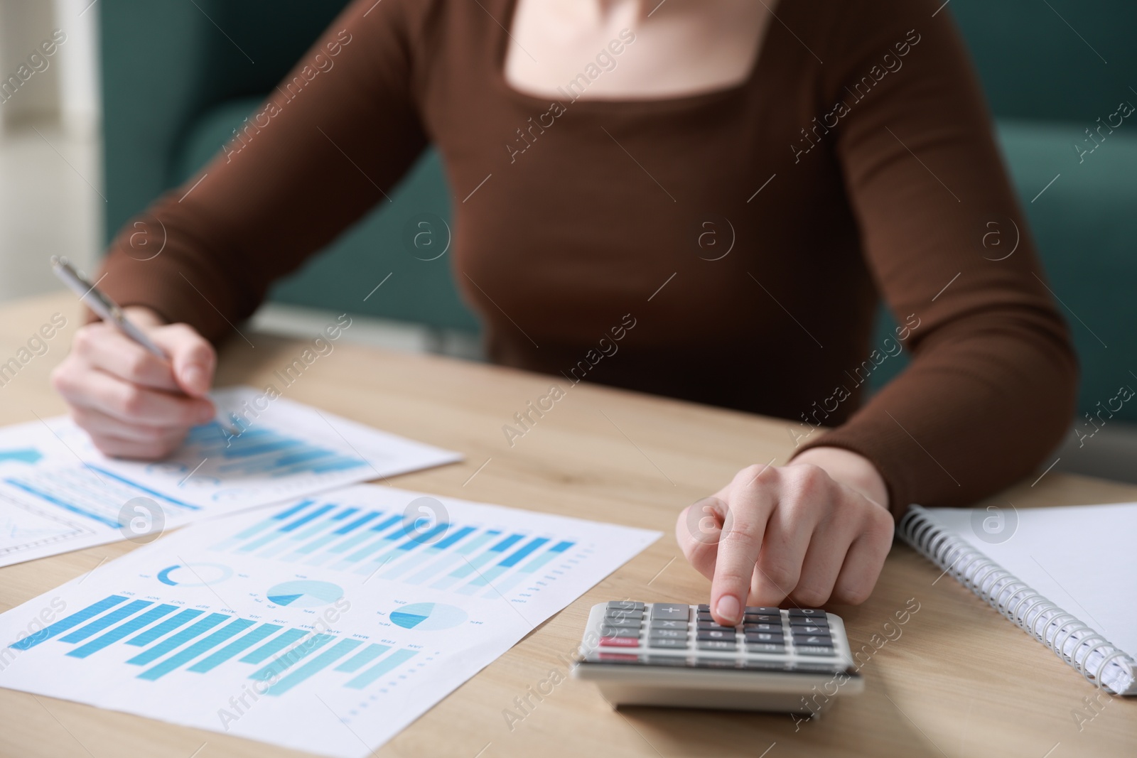 Photo of Budget. Woman with paperwork and calculator at wooden desk indoors, closeup