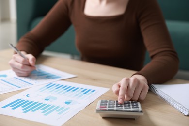 Photo of Budget. Woman with paperwork and calculator at wooden desk indoors, closeup