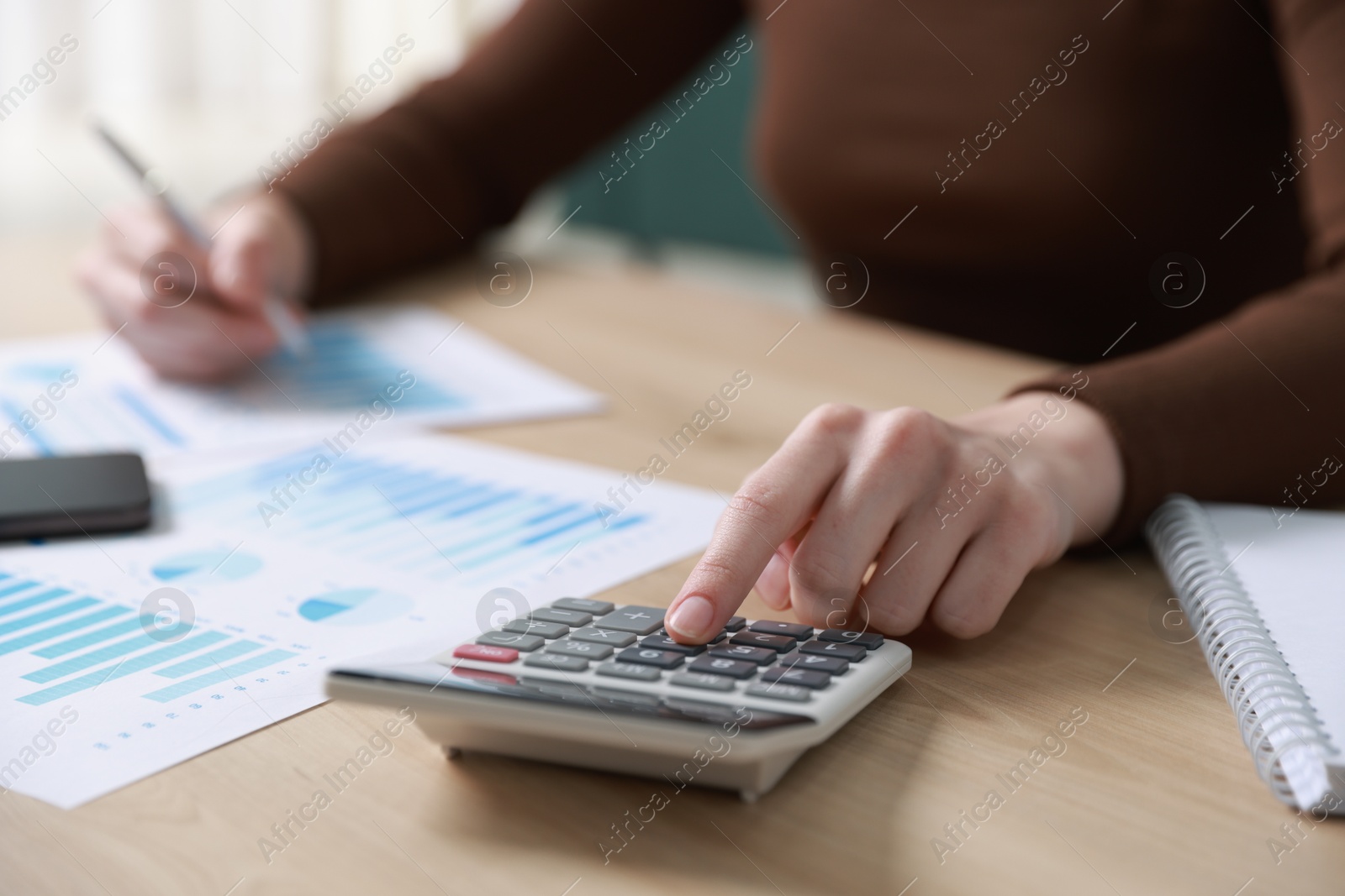 Photo of Budget. Woman with paperwork and calculator at wooden desk indoors, closeup