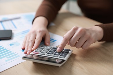 Photo of Budget. Woman with paperwork and calculator at wooden desk indoors, closeup