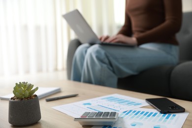 Photo of Budget. Paperwork, calculator on wooden desk and woman working with laptop indoors, selective focus