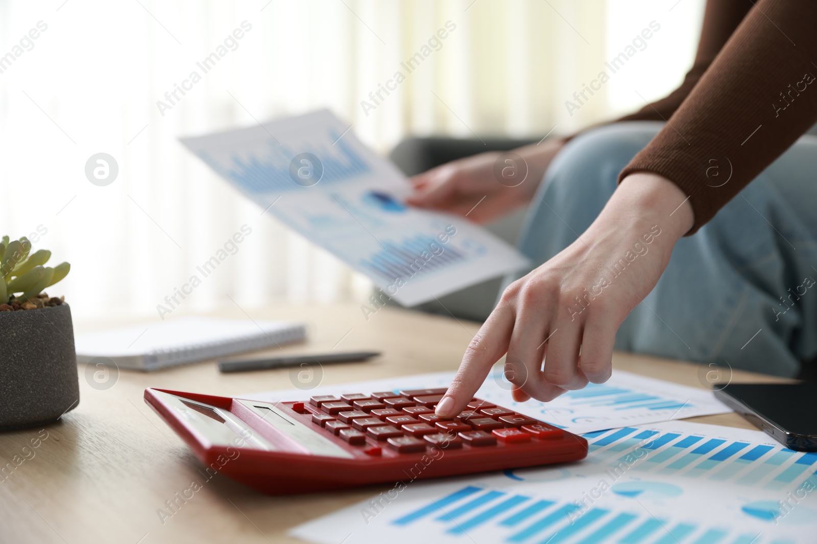 Photo of Budget. Woman with paperwork and calculator at wooden desk indoors, closeup