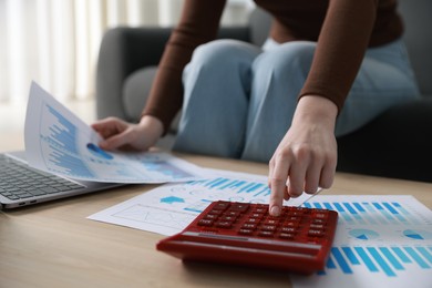 Photo of Budget. Woman with paperwork and calculator at wooden desk indoors, closeup