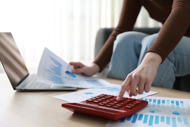 Photo of Budget. Woman with paperwork and calculator at wooden desk indoors, closeup