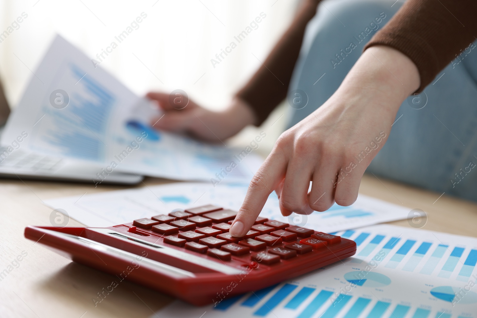 Photo of Budget. Woman with paperwork and calculator at wooden desk indoors, closeup