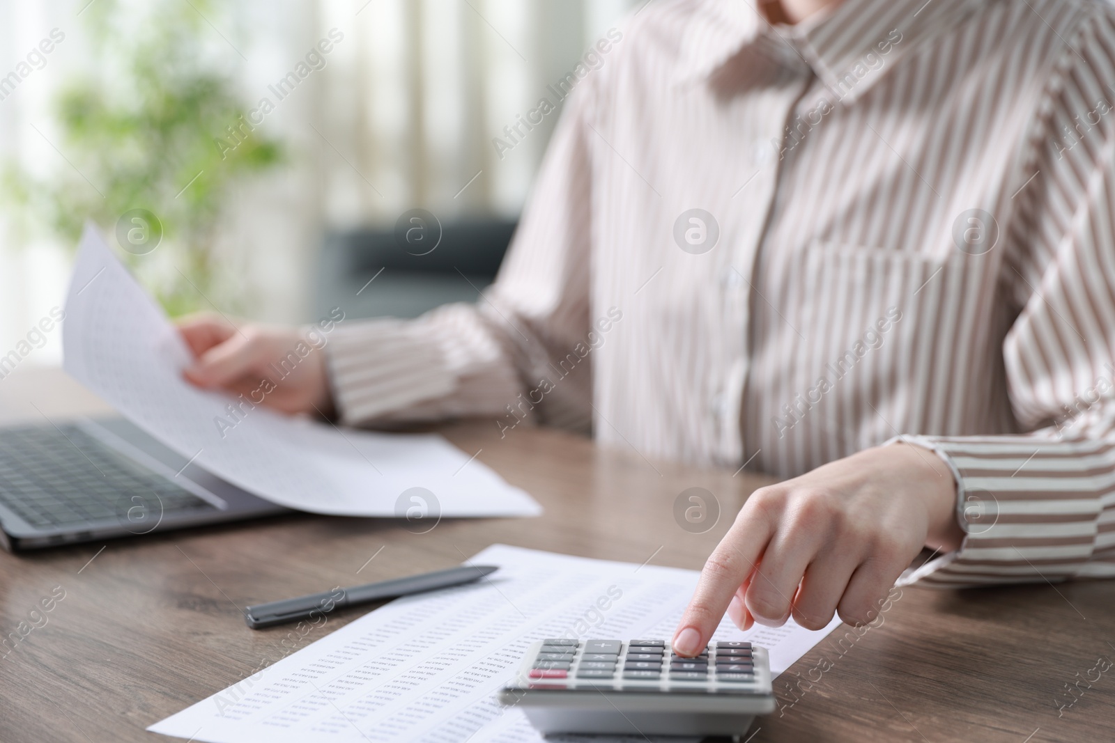 Photo of Budget. Woman with paperwork and calculator at wooden desk indoors, closeup